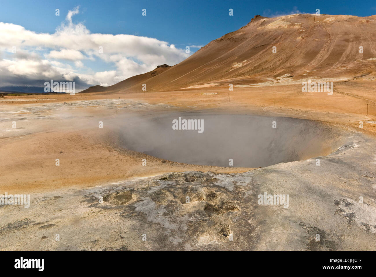 A big boiling mud puddle emits smoke and it's surrounded by the warm orange ground, characteristic of the Hiverir area, Iceland Stock Photo