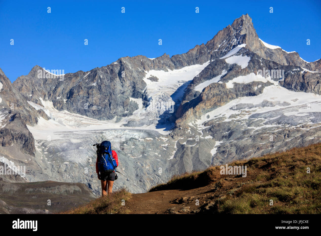 Hiker proceeds on the footpath towards the high peaks in a clear summer day Gornergrat Canton of Valais Switzerland Europe Stock Photo