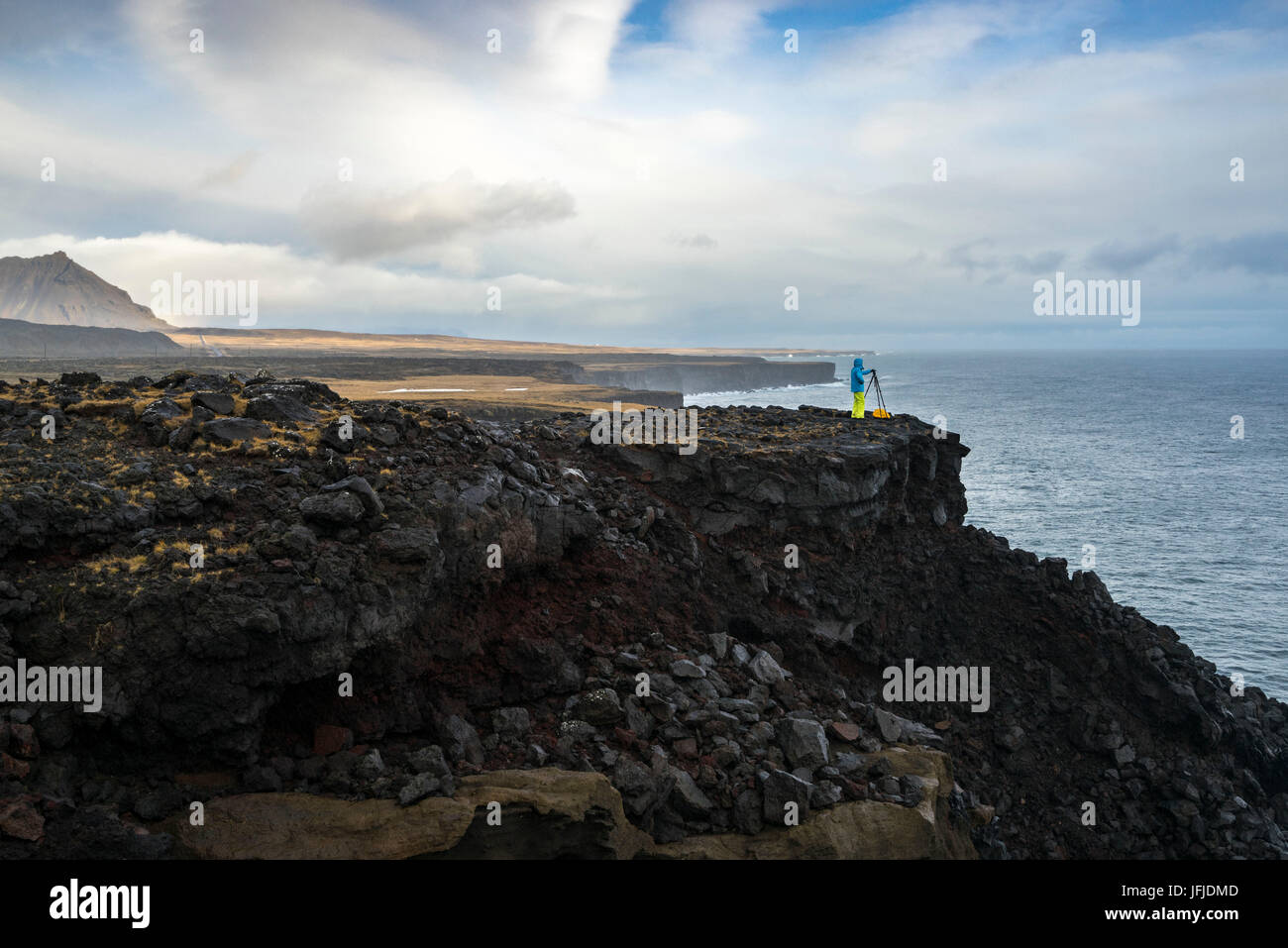 A photographer is taking pictures with tripod standing on the cliffs near Londrangar, Snaefellsjoekull National Park, Western Iceland, Europe Stock Photo