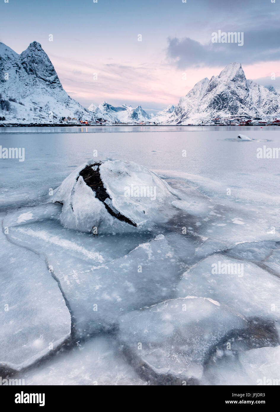 The frozen sea and the snowy peaks frame the fishing village at sunset
