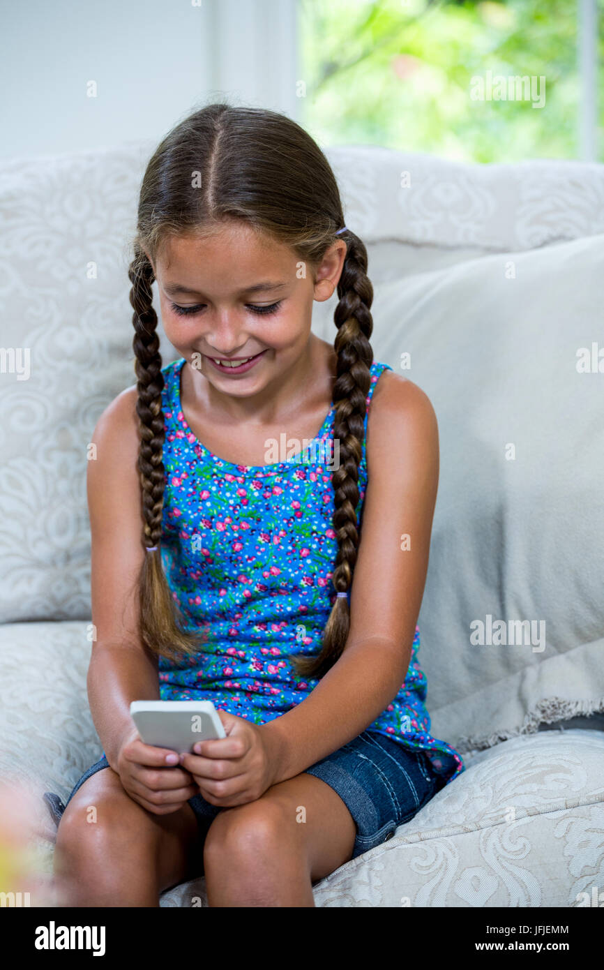 Girl using mobile phone while sitting on sofa at home Stock Photo - Alamy
