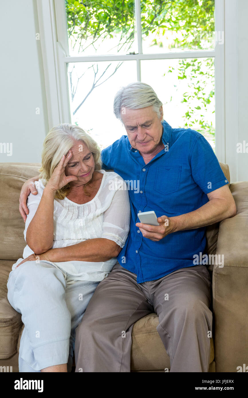 Serious senior couple using mobile phone while sitting on sofa Stock ...