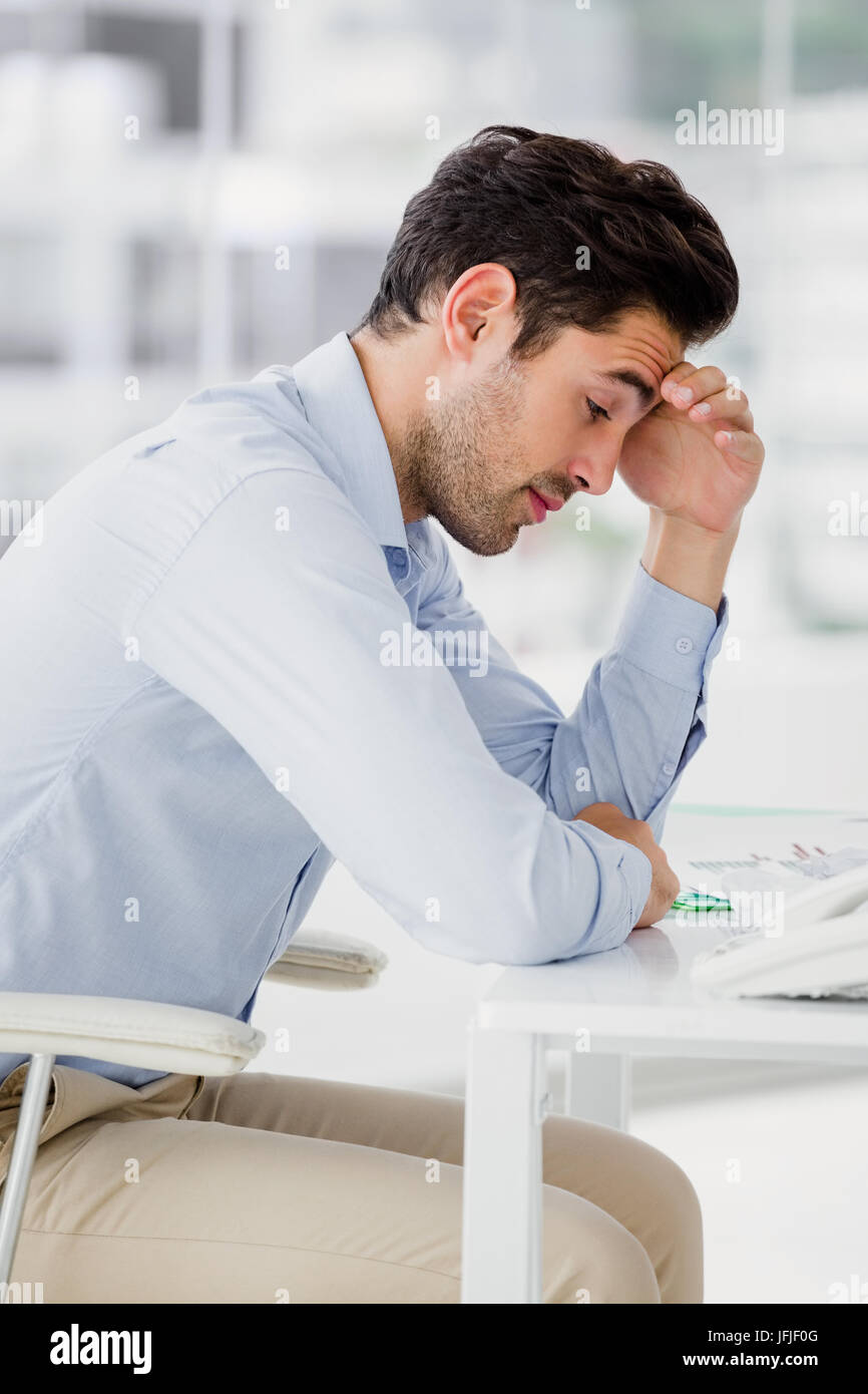 Frustrated businessman sitting on desk with hand on head Stock Photo