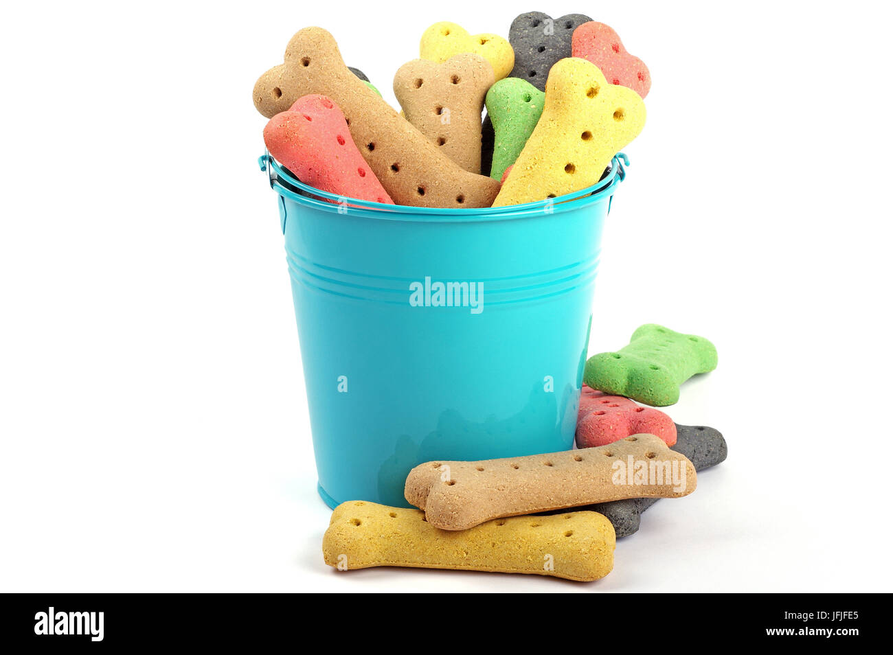 a mixture of coloured dog biscuits in a blue bucket on a white background with scattered loose biscuits around bottom of bucket Stock Photo