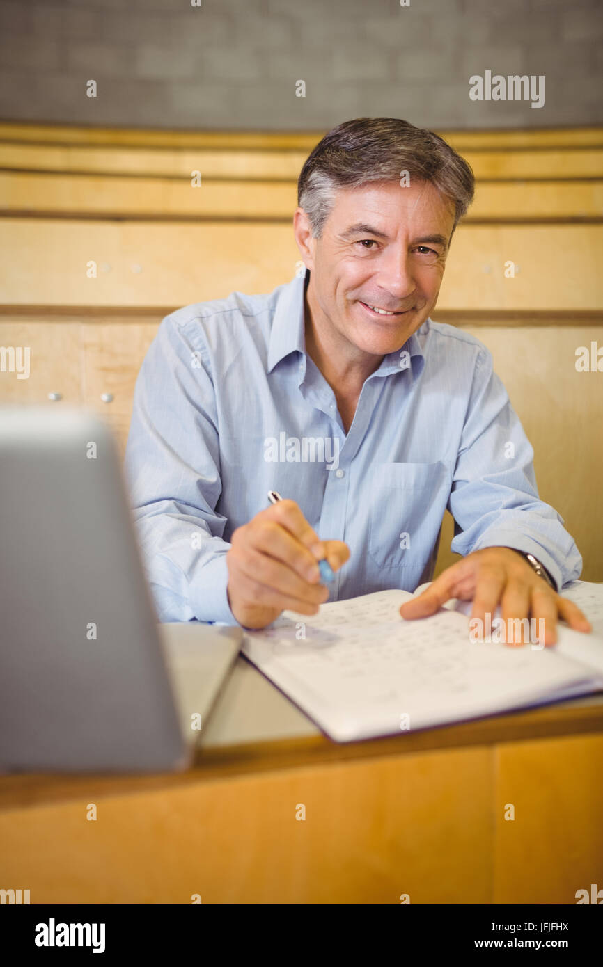Portrait of happy professor writing in book at desk Stock Photo