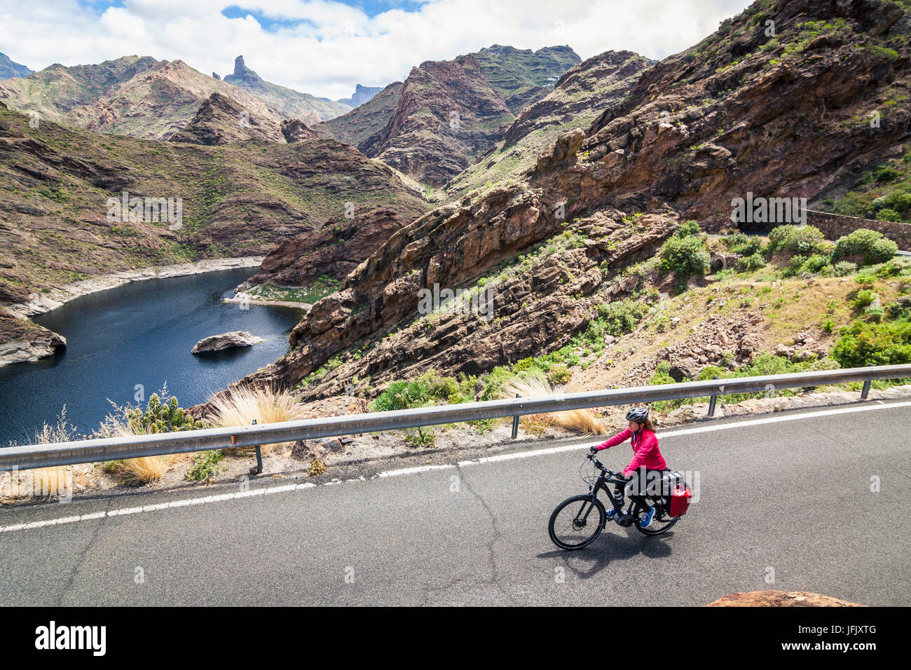 Mountain biker riding electric bicycle on road against mountain range Stock Photo