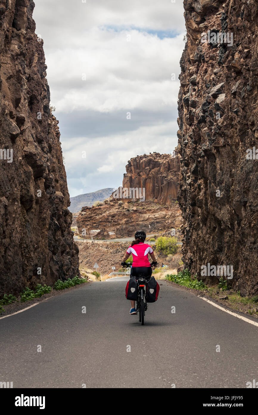 Rear view of woman riding electric bicycle on road amidst mountains Stock Photo