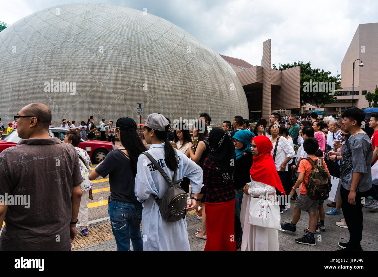 Tourists and locals waiting at Tsim Sha Tsui intersection to cross street, dome of Hong Kong Space Museum in background Stock Photo