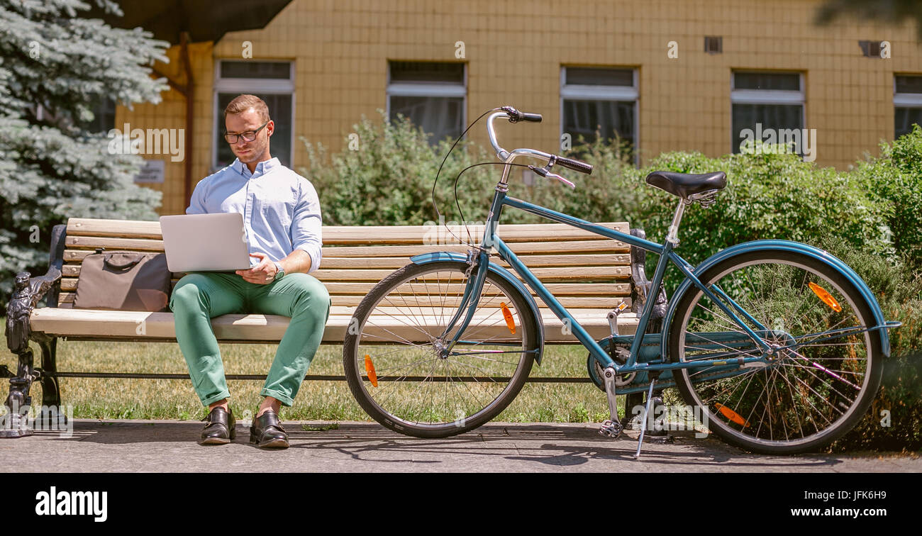 Businessman working on laptop sitting on a bench, next to a bicycle Stock Photo