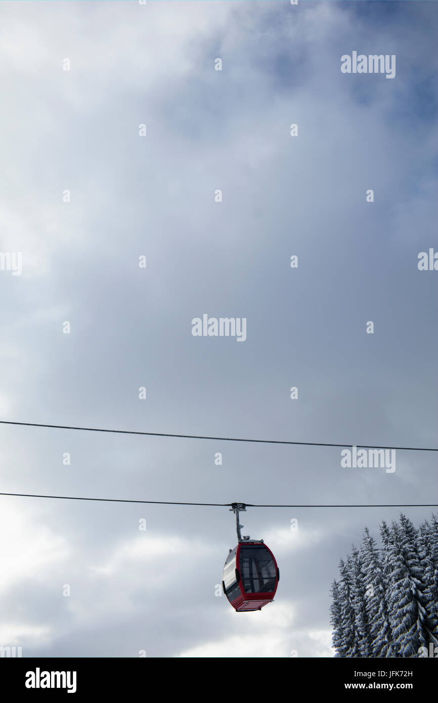 Low angle view of overhead cable car with snowcapped pine trees against cloudy sky Stock Photo