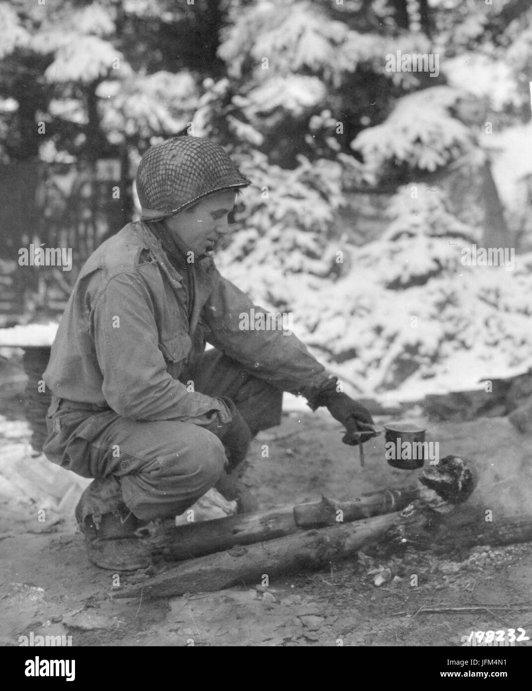 Pvt Floyd Corum heats coffee in a canteen cup over a log fire after a heavy snowfall. ETO, 12/22/44, Belgium Stock Photo
