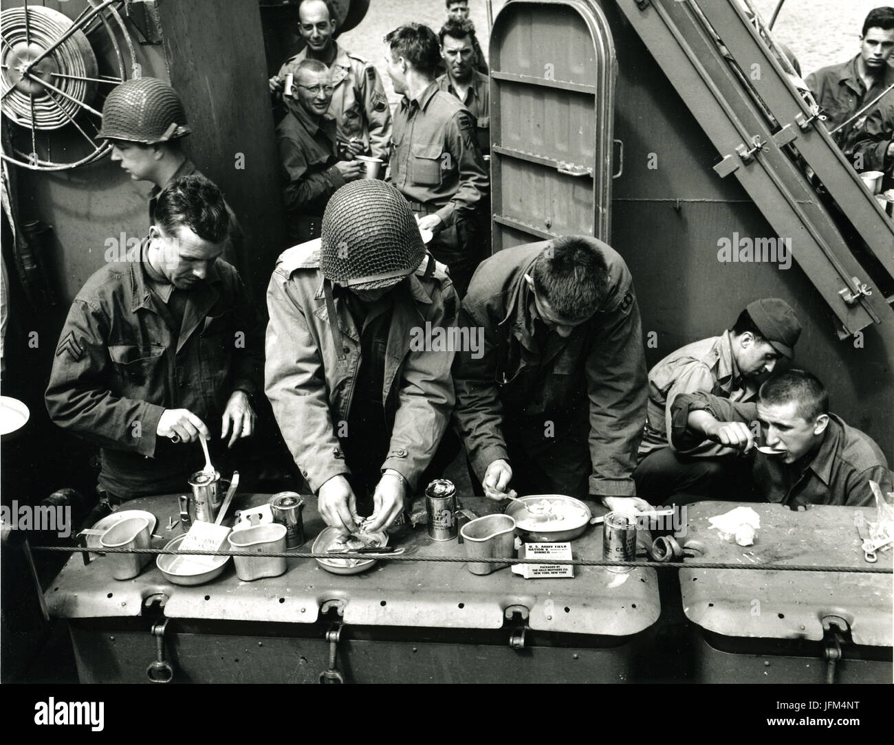 Crossing the English Channel aboard a Coast Guard 'Elsie' (or LCI), American soldiers catch their K rations and celery soup from the top of a 20 mm ready box. Ahead lies the coast of France, but for the moment chow is the important thing. You can't fight on a hollow stomach. June 6, 1944 Stock Photo