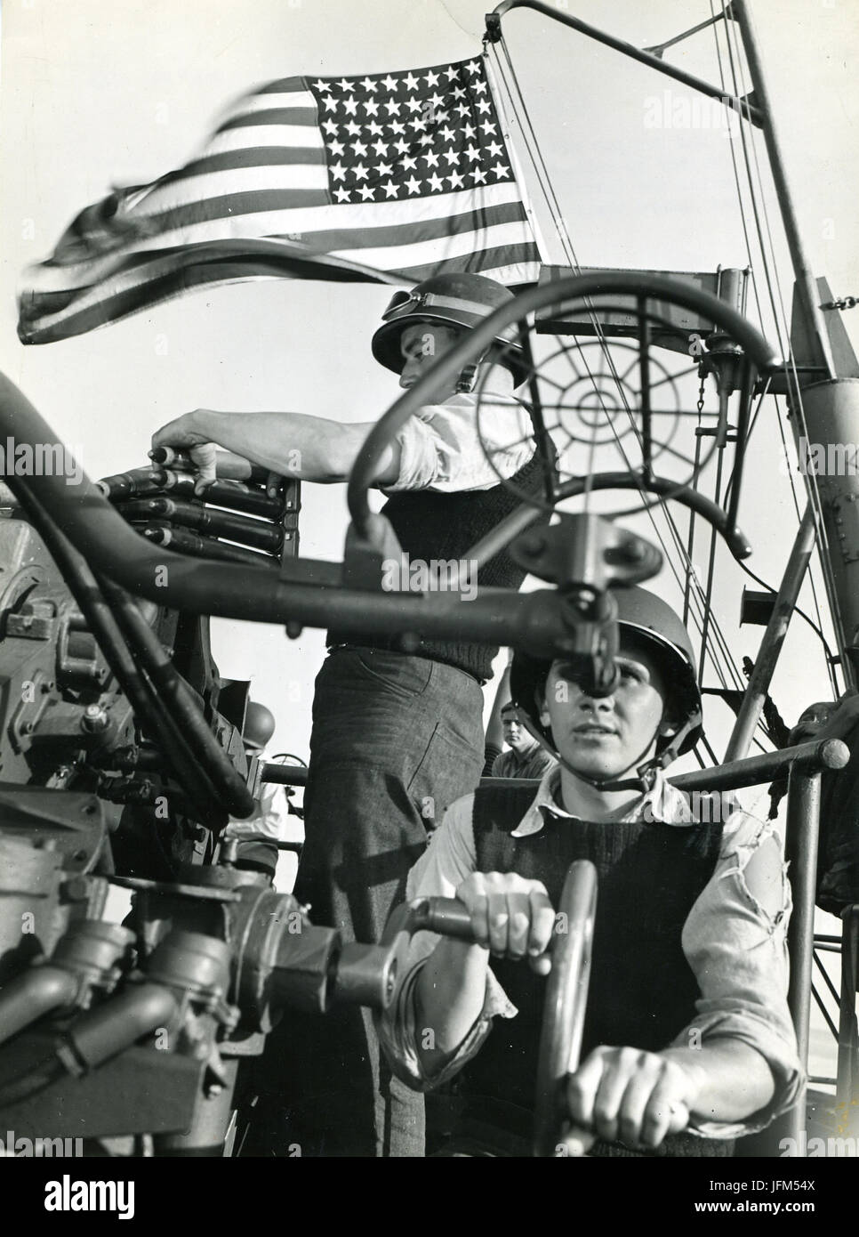 July 28, 1943 - The Stars and Stripes wave triumphantly as a trainer and loader aboard an American cruiser go methodically about their work during the bombardment which accompanied the invasion of Sicily. Stock Photo