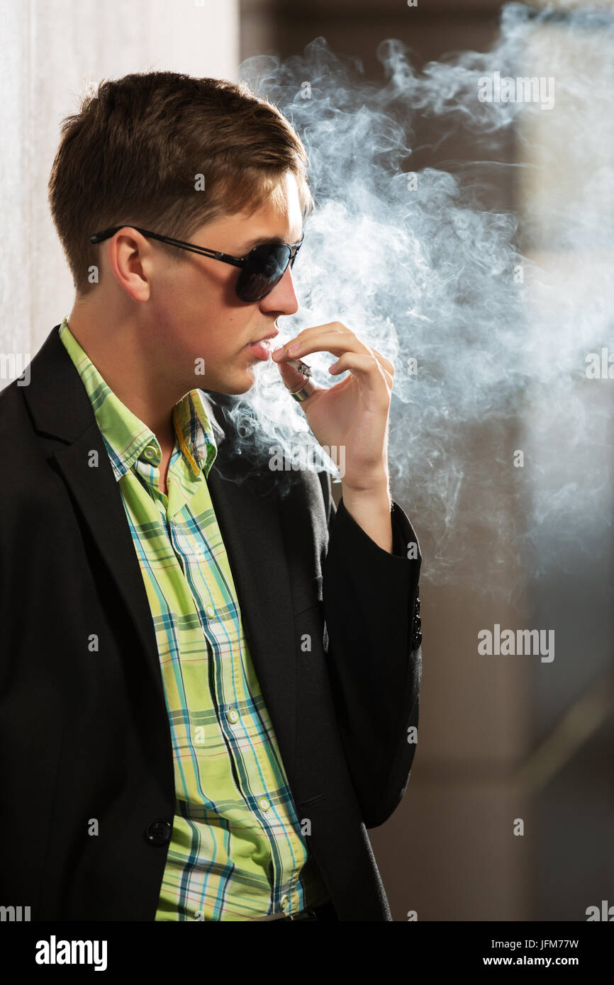 Young fashion man in sunglasses smoking a cigarette Stock Photo