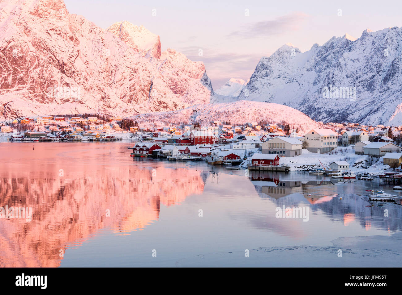 Pink sunrise and snowy peaks frame the frozen sea and the fishing village Reine Bay Nordland Lofoten Islands Norway Europe Stock Photo