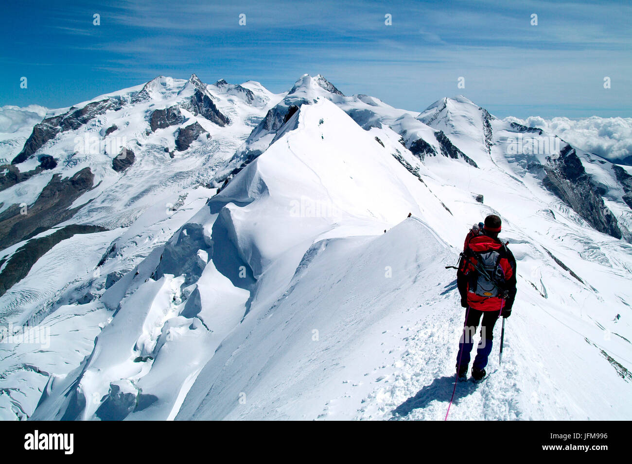 A hiker contemplating the breathtaking view from the Breithorn summit, in the Mount rosa Massif, with the Lyskamm, Castor, Pollux, on the border between Italy and Switzerland Europe Stock Photo