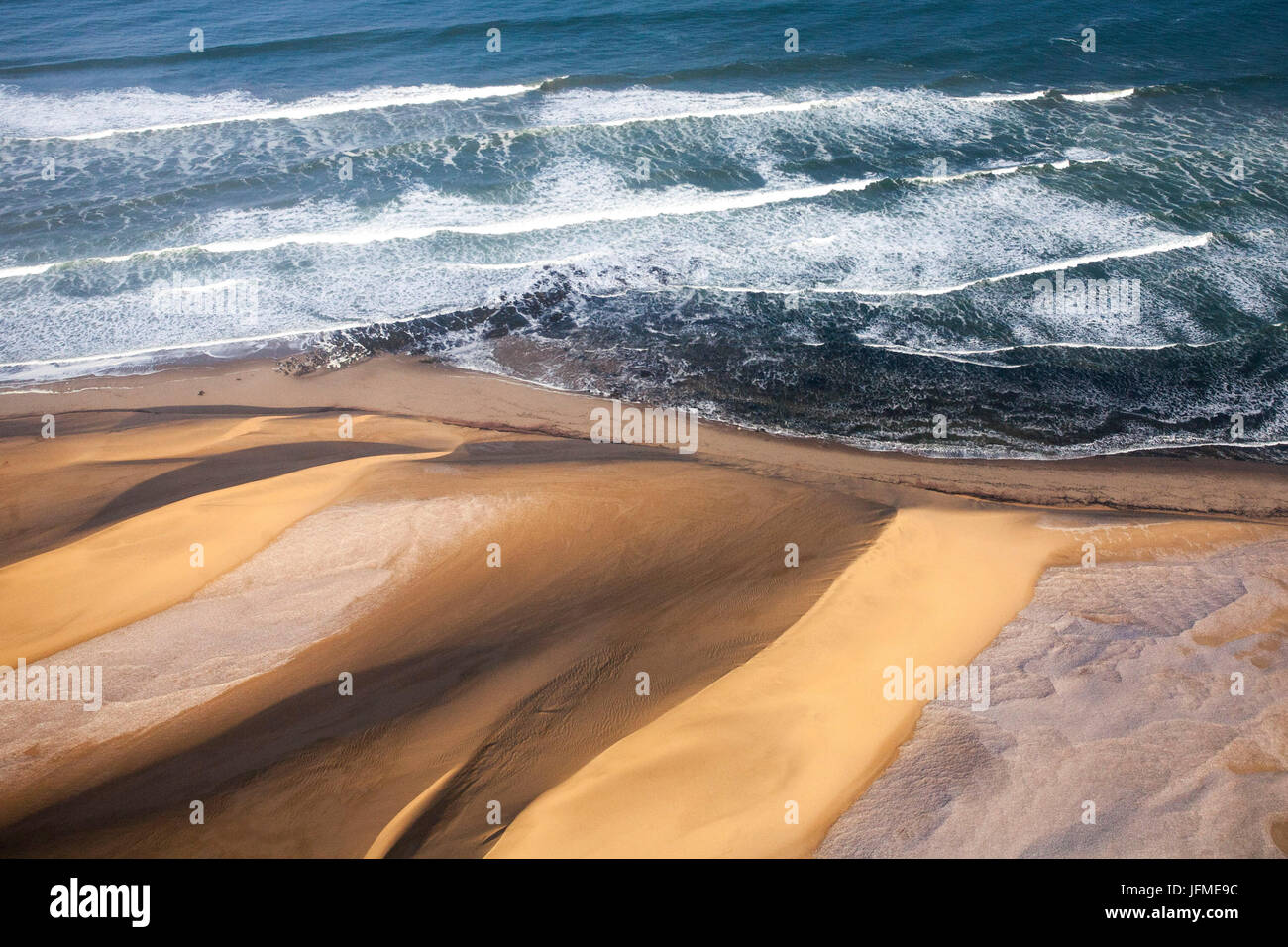 Aerial view of waves of the Atlantic Ocean crashing against the sandy dunes of the Namib desert Namibia Southern Africa Stock Photo