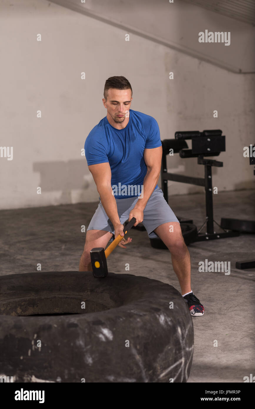 Sledgehammer Tire Hits young muscular man workout at gym with hammer