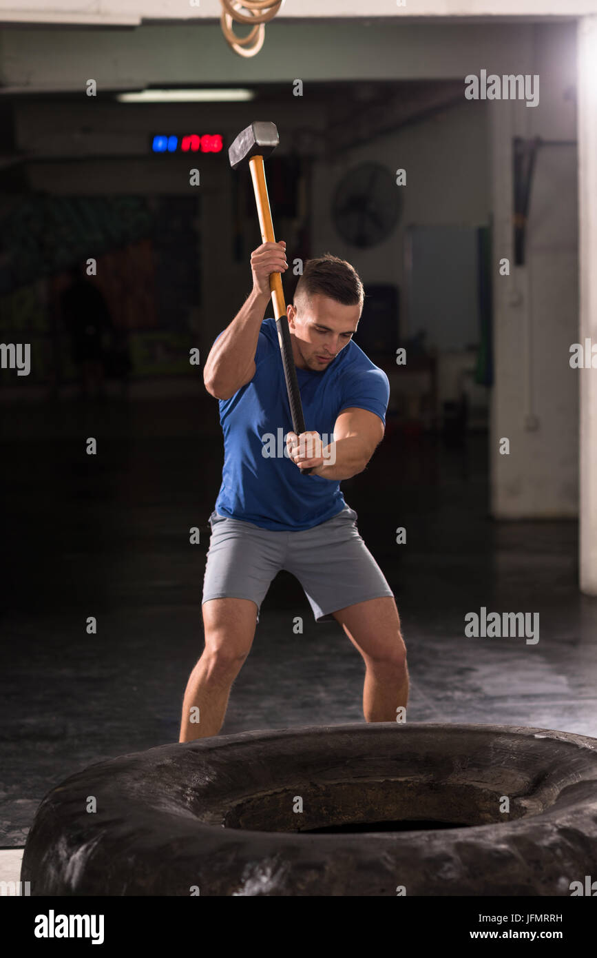Sledgehammer Tire Hits young muscular man workout at gym with hammer