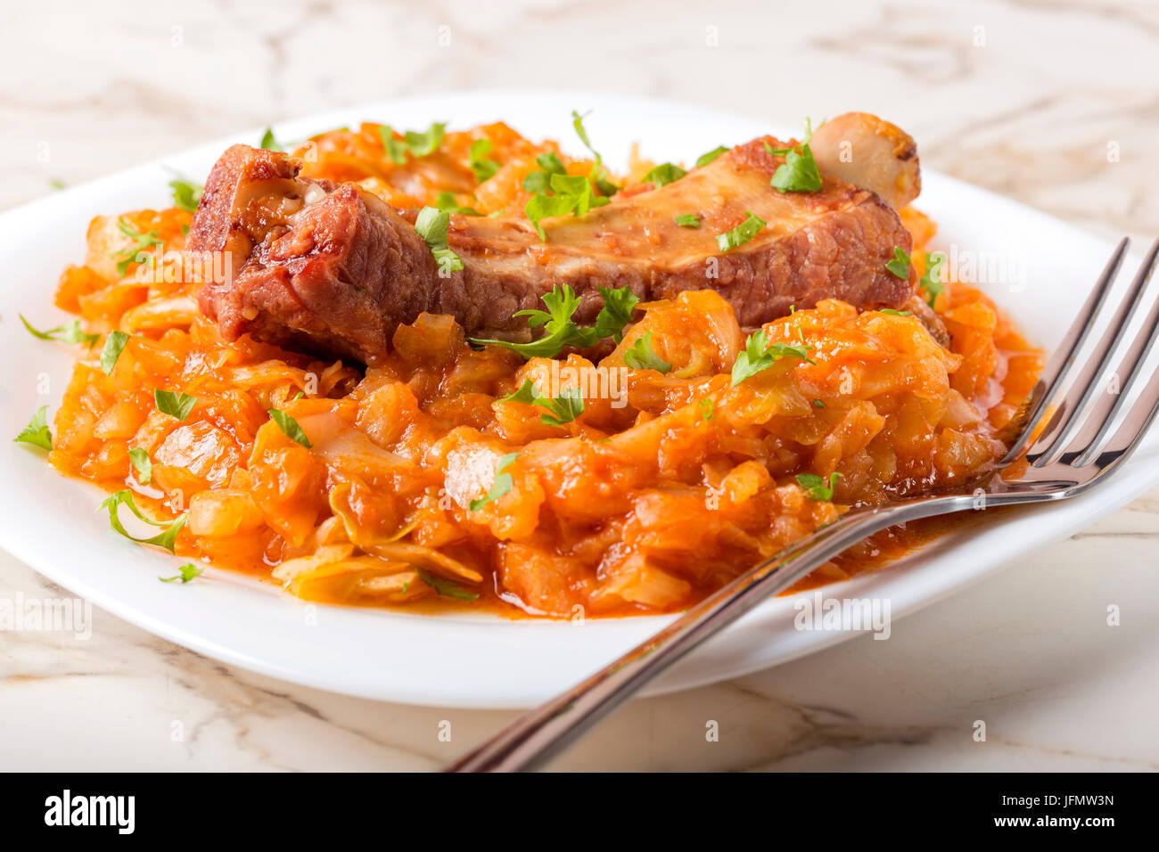 Cabbage cooked with Smoked Pork Ribs and green parsley Served in white plate with fork Stock Photo