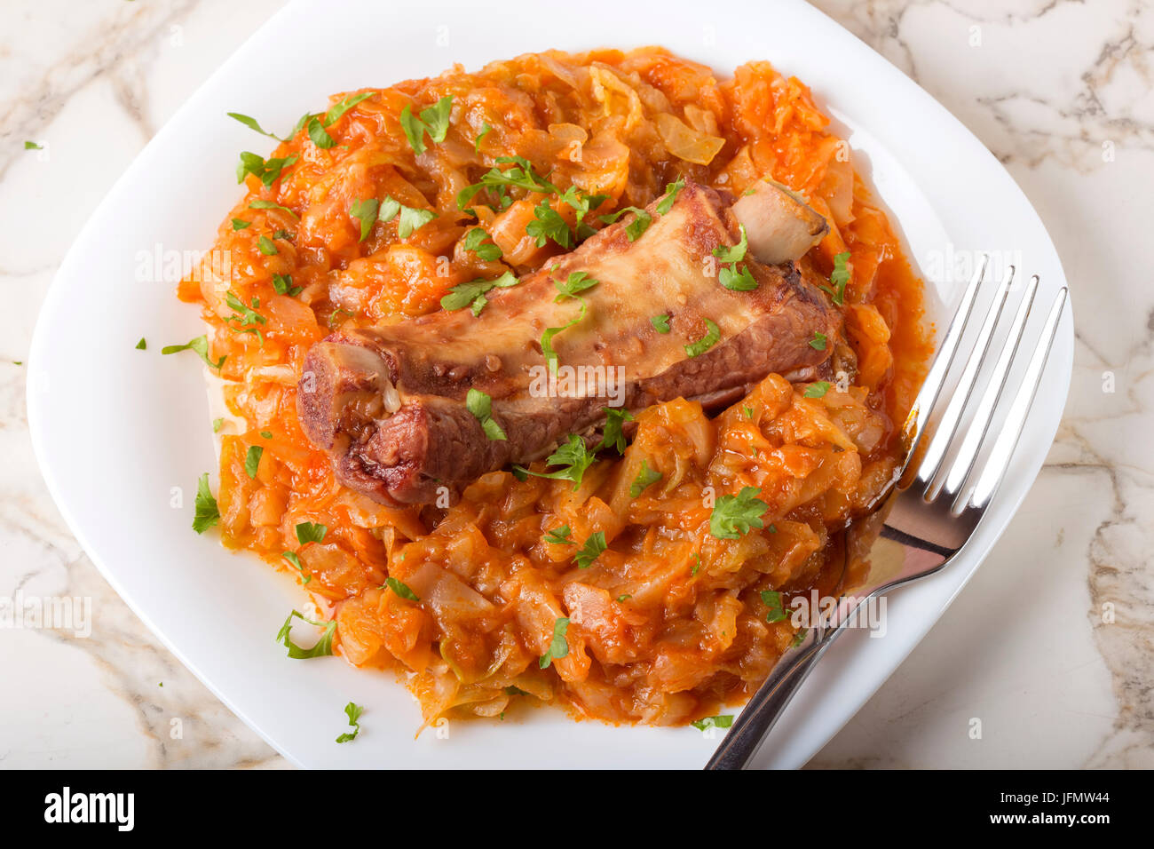 Cabbage cooked with Smoked Pork Ribs and green parsley Served in white plate with fork Stock Photo