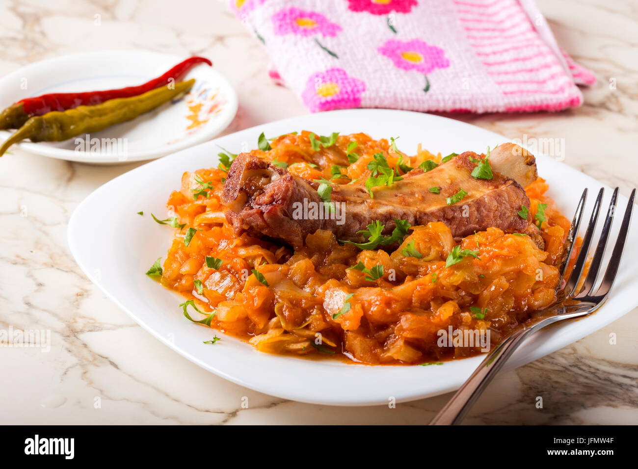 Cabbage stew with Smoked Pork Ribs and green parsley Served in white plate with pickled chili peppers Stock Photo