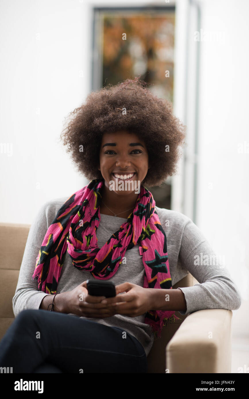 young happy african american woman sitting on sofa and using mobile ...