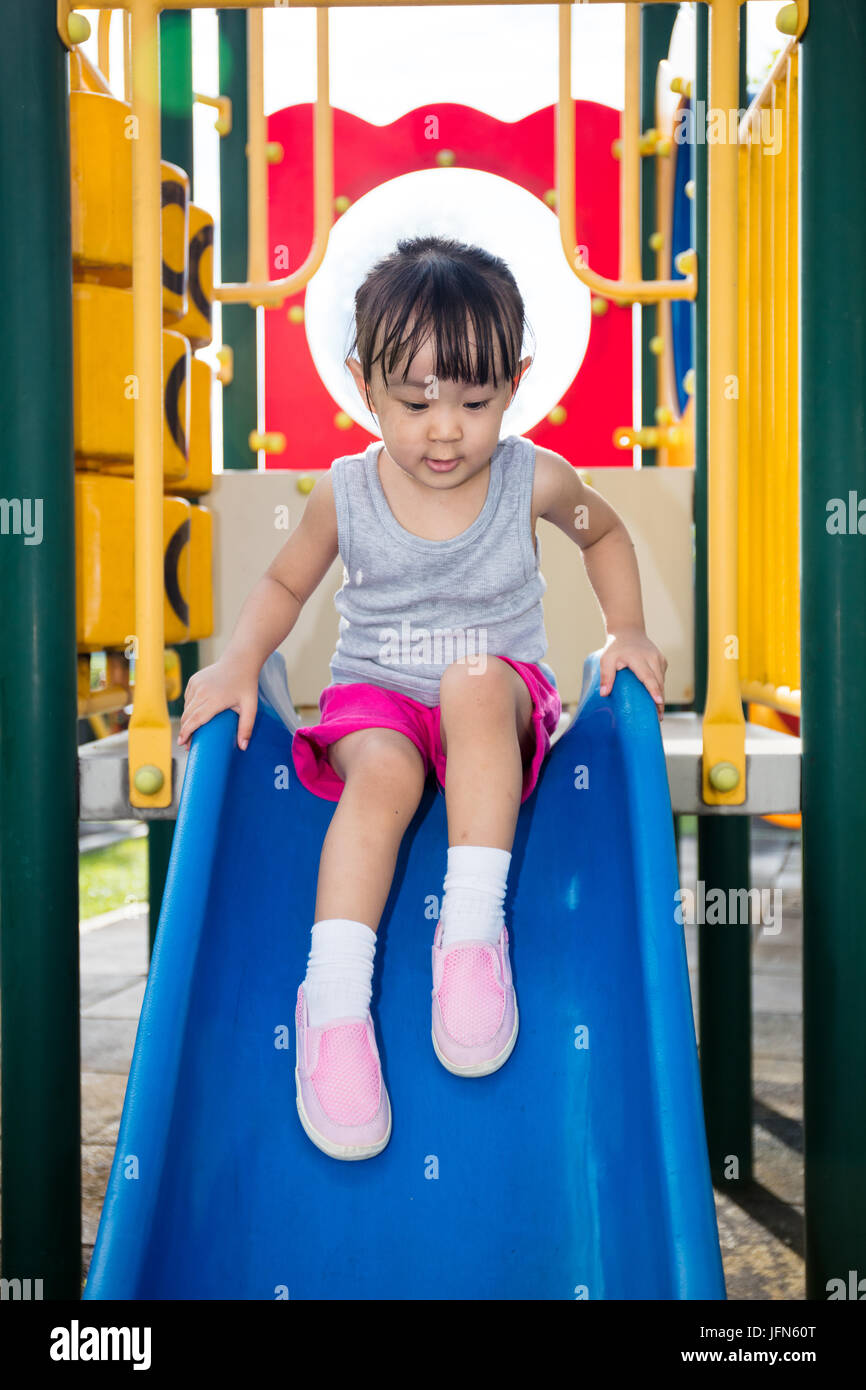 Asian Chinese little girl playing on the slide at outdoor playground ...