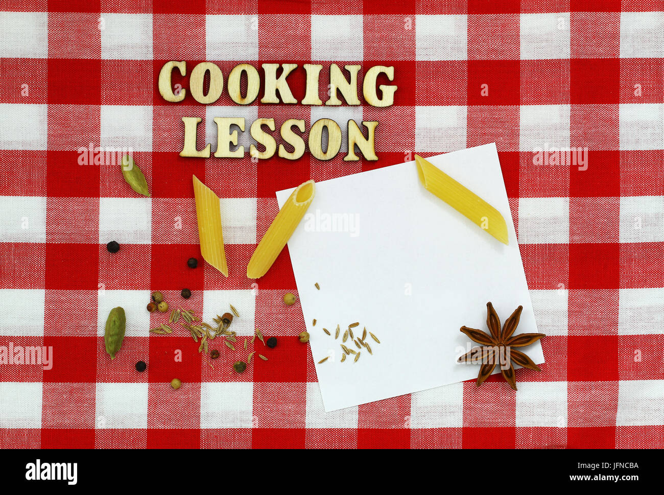 Cooking lesson written with wooden letters on checkered cloth, raw pasta, spices and white pieces of paper Stock Photo