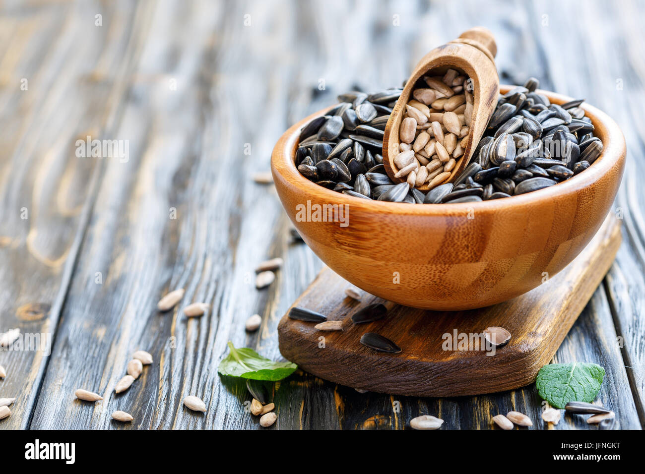 Wooden scoop with cleaned seeds in bowl with sunflower seeds. Stock Photo