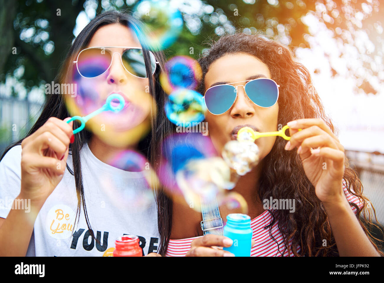 Two young girlfriends wearing sunglasses having fun together blowing