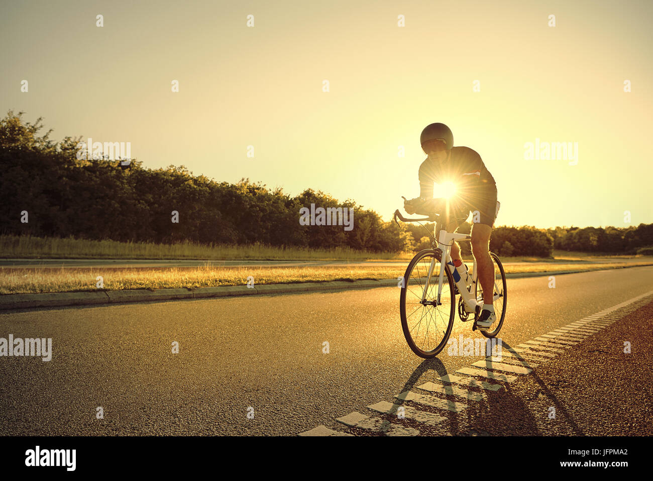 The cyclist moving on a bike on an empty highway in the sunset lights. Stock Photo