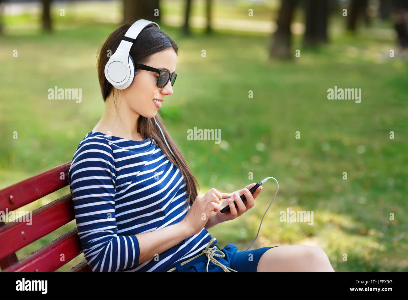 Young woman with headphones and smartphone outdoors on summer day. Girl listening music in headphones in park Stock Photo