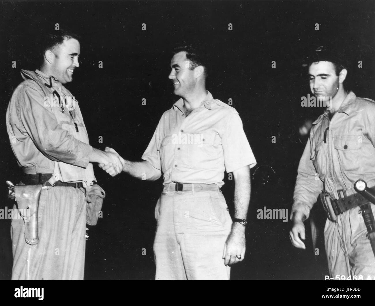 Major Charles W. Sweeney (left), pilot of the B-29 BOCKSCAR which dropped the atomic bomb on Nagasaki on August 9, 1945, is shown before his mission shaking hands with Col Paul W. Tibbets, pilot of ENOLA GAY which atom bombed Hiroshima on 6 August 1945. Man at right is Capt James Van Pelt, navigator for Maj Sweeney. Tinian, August 9, 1945 Stock Photo