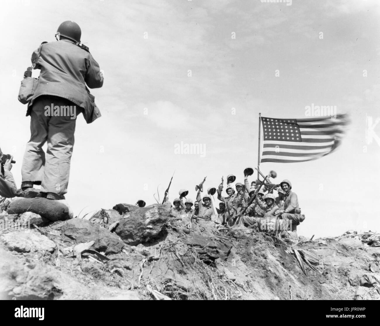 In a stiff breeze atop Mount Suribachi, volcano mountain on Iwo Jima Island, the American flag whips against the sky as cheering Marine raise their voices and weapons in the historic moment for a photograph, Iwo Jima, February 1945. USMC Photo by Bob Campbell Stock Photo