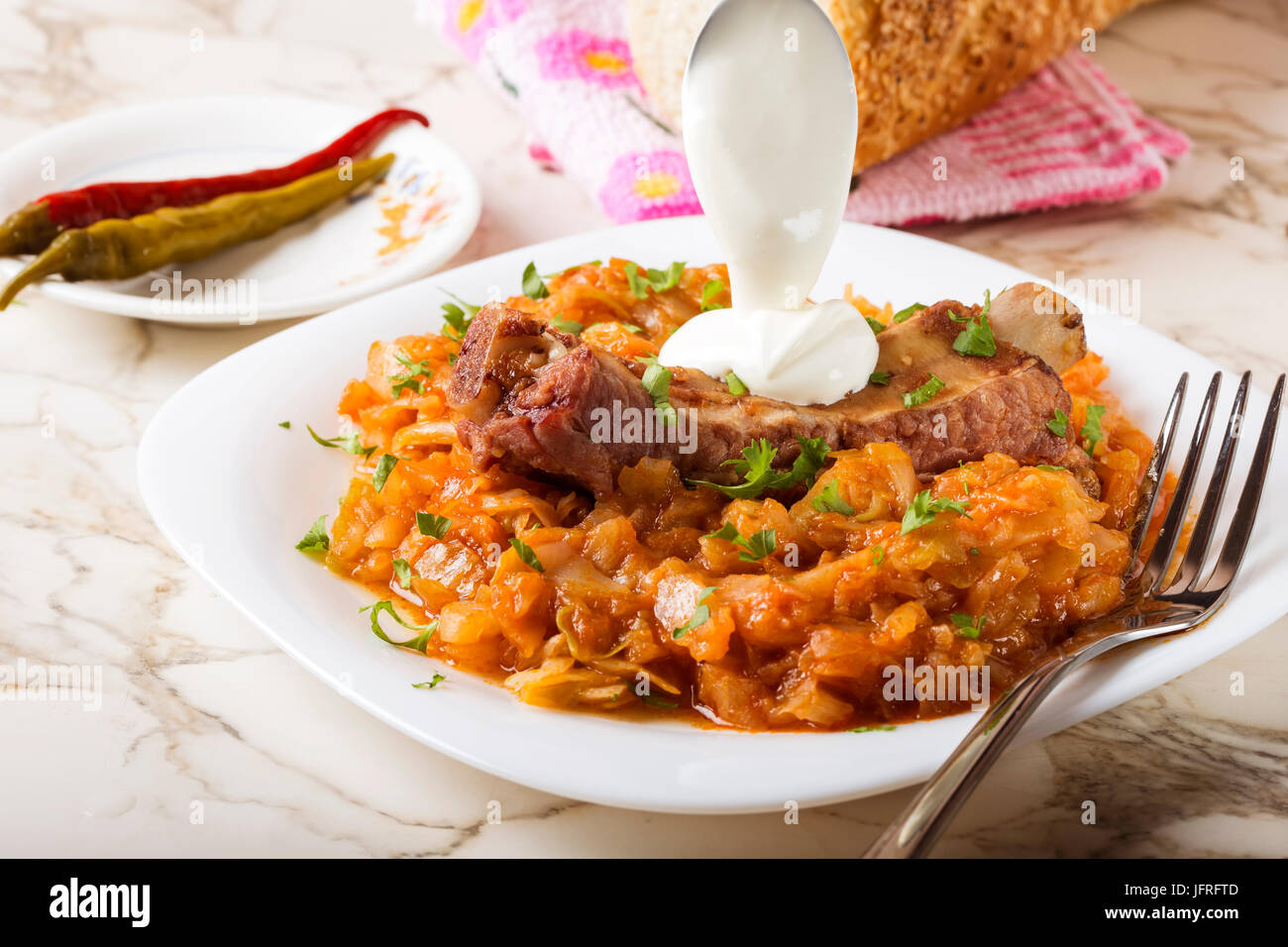 Cabbage stew with Smoked Pork Ribs, cream  and green parsley Served in white plate with pickled chili peppers and bread Stock Photo