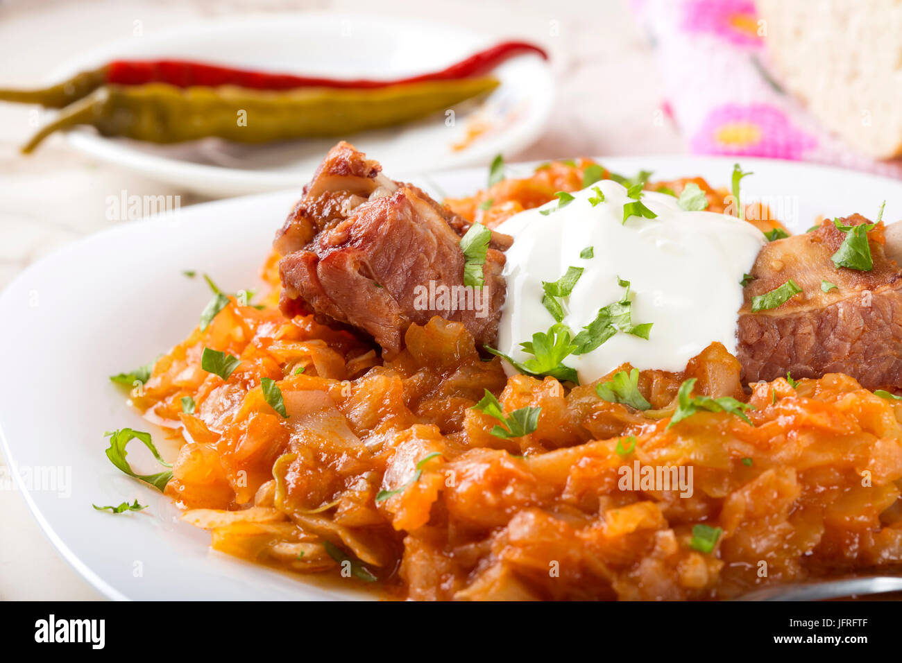 Cabbage stew with Smoked Pork Ribs, cream and green parsley Served in white plate with pickled chili peppers Stock Photo