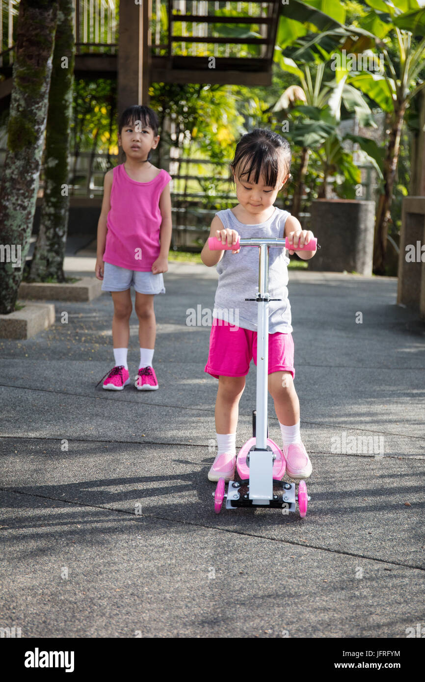 Asian little Chinese girls arguing to play the scooter at outdoor park Stock Photo