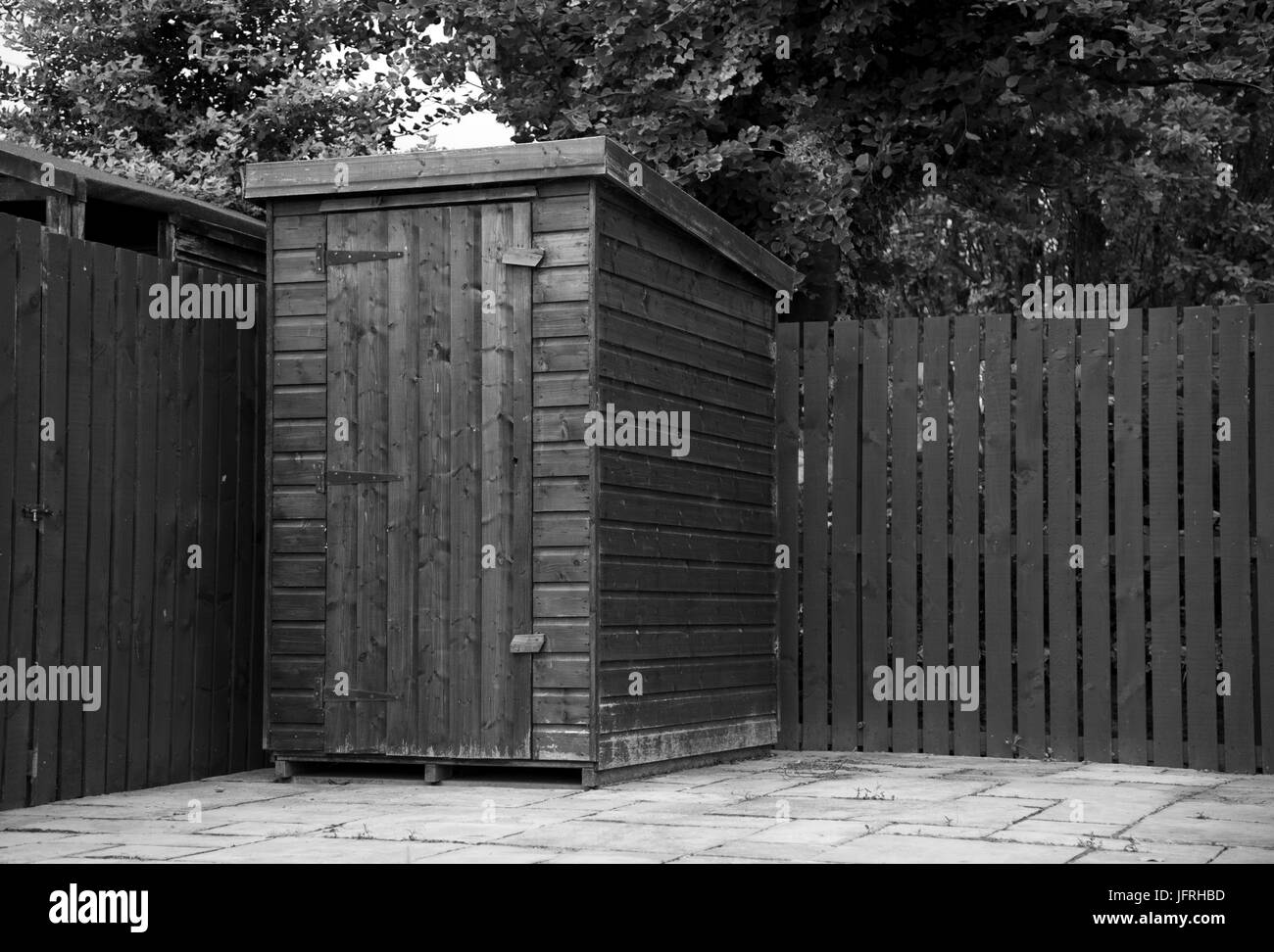 Black and White image of a small wooden garden shed on a patio in the corner of a garden on a dull Summer's day. Stock Photo