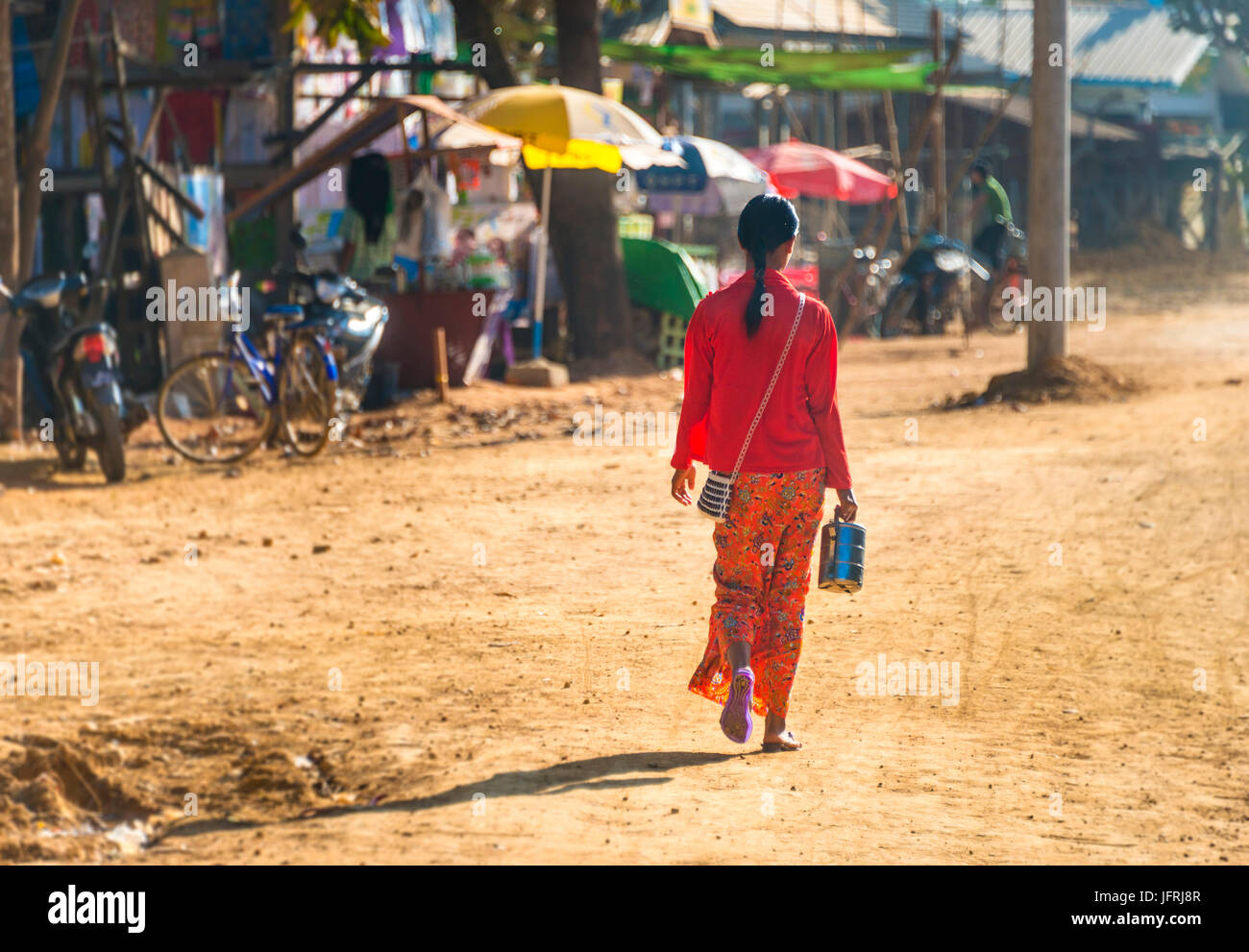 Young indigenous woman in colorful traditional robe walking, street scene, Chaung Tha Beach, Myanmar Stock Photo