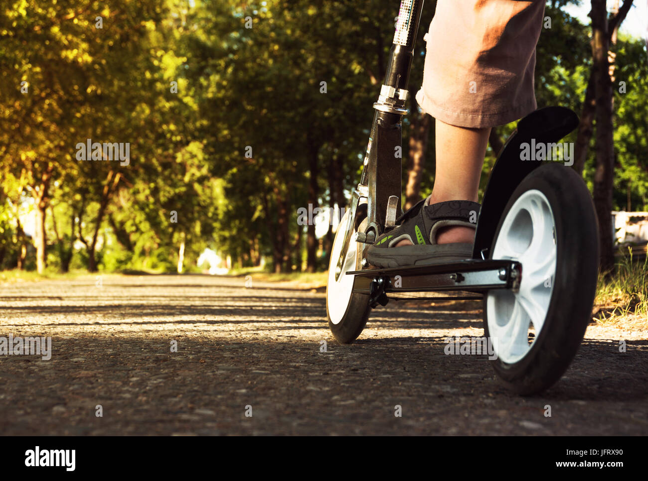 Child's feet in sandals standing on the scooter. black scooter wheels. at scooter's Stock Photo