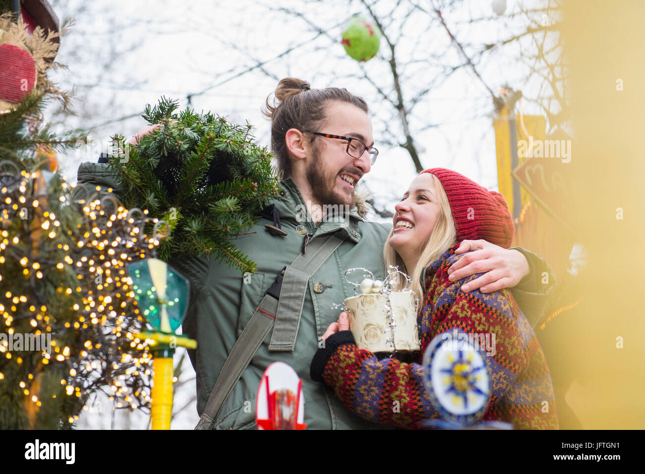 Young man carrying Christmas tree and embracing his girlfriend Stock