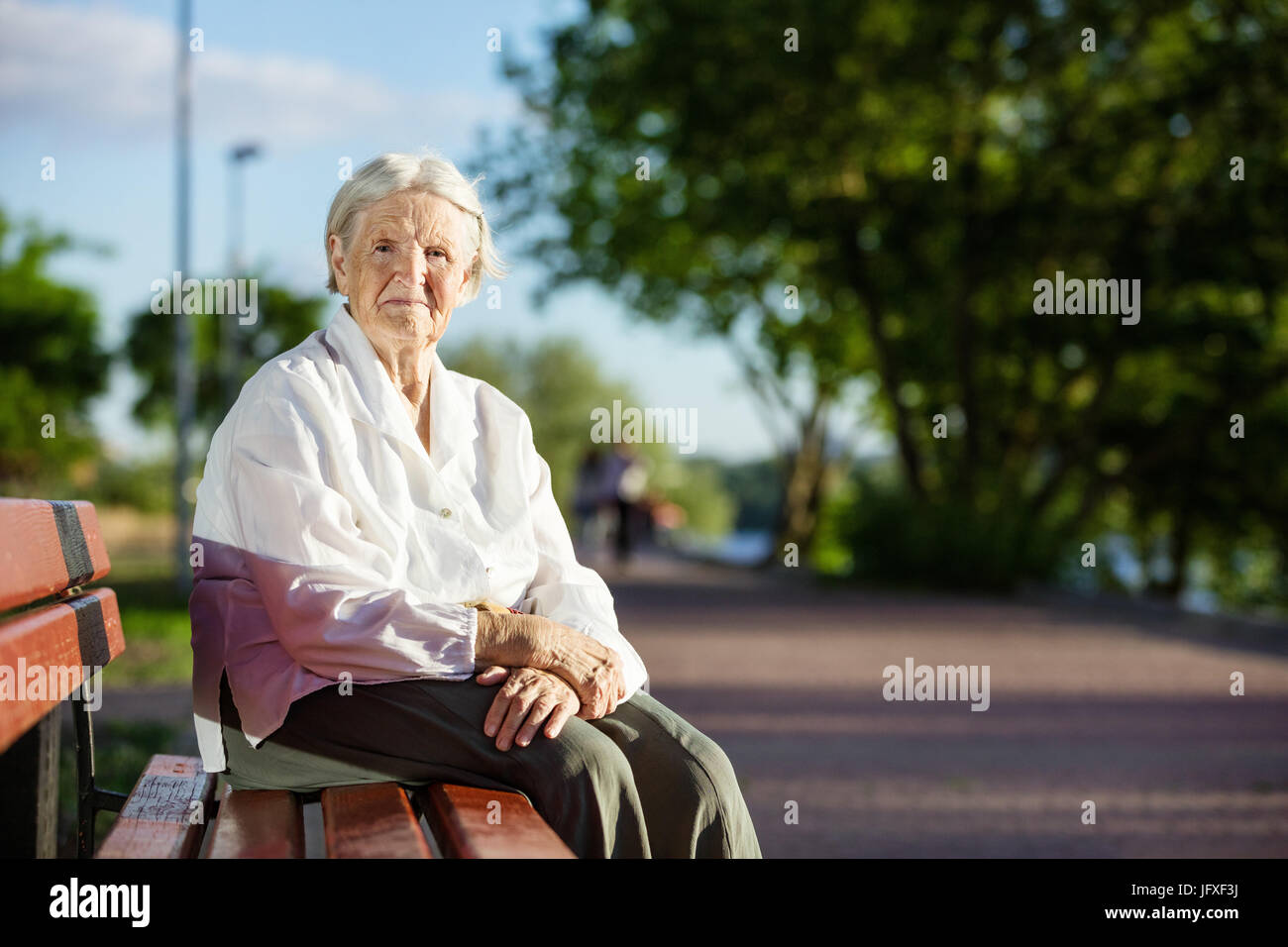 Senior woman sitting on bench in park and smiling Stock Photo - Alamy