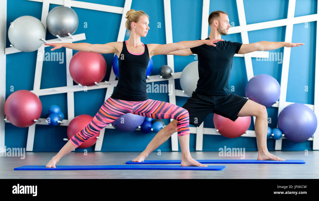 Nice couple doing yoga in a studio. Young people in yoga class in Warrior pose. Yoga group concept. Stock Photo