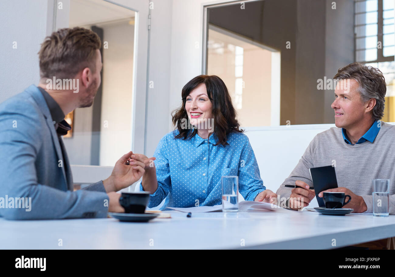 Three smiling work colleagues talking business together in an office Stock Photo