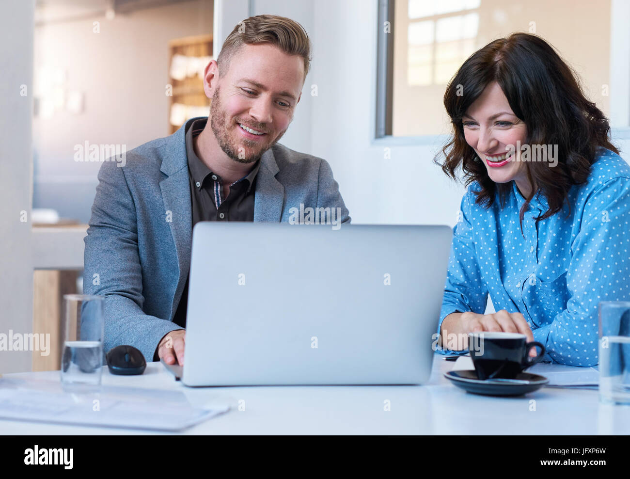 Two smiling young coworkers using a laptop in an office Stock Photo