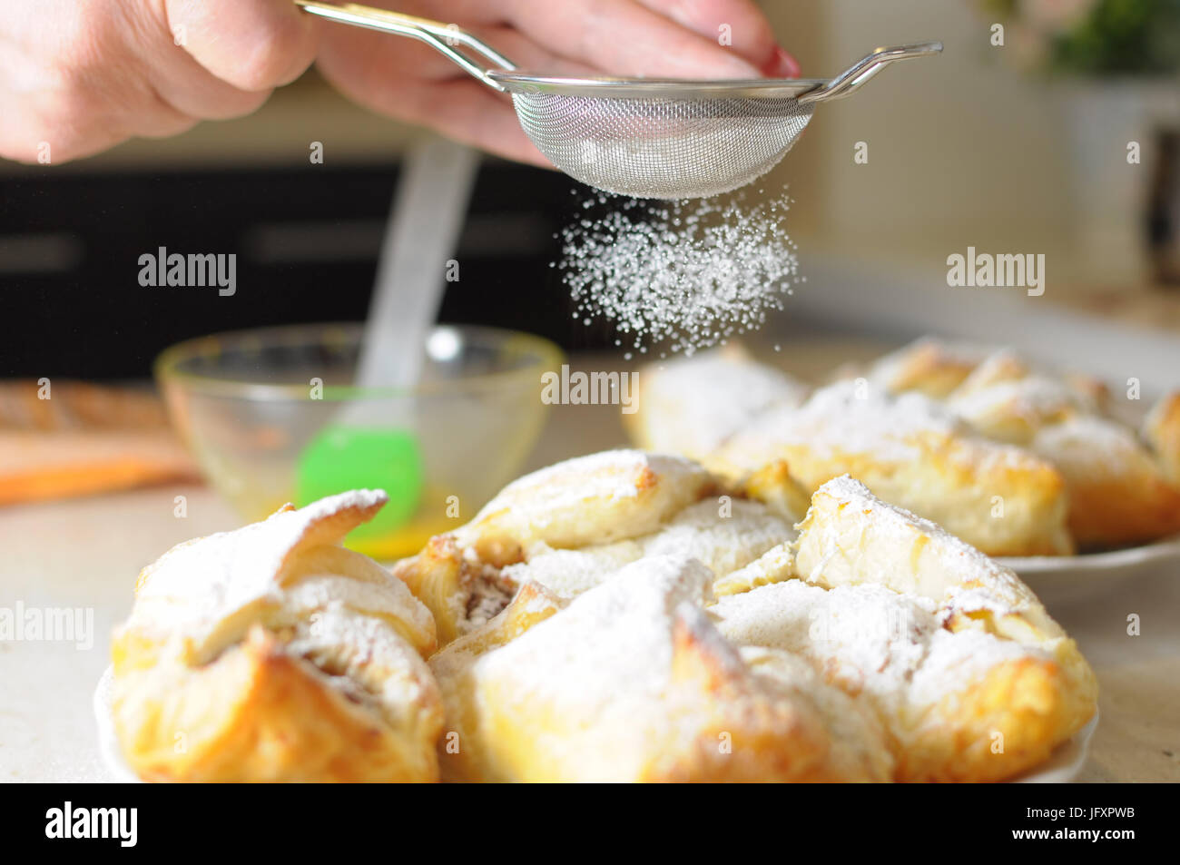 Female hands sprinkle powdered sugar on apple puffs. Process of cooking close up. Selective focus. Stock Photo