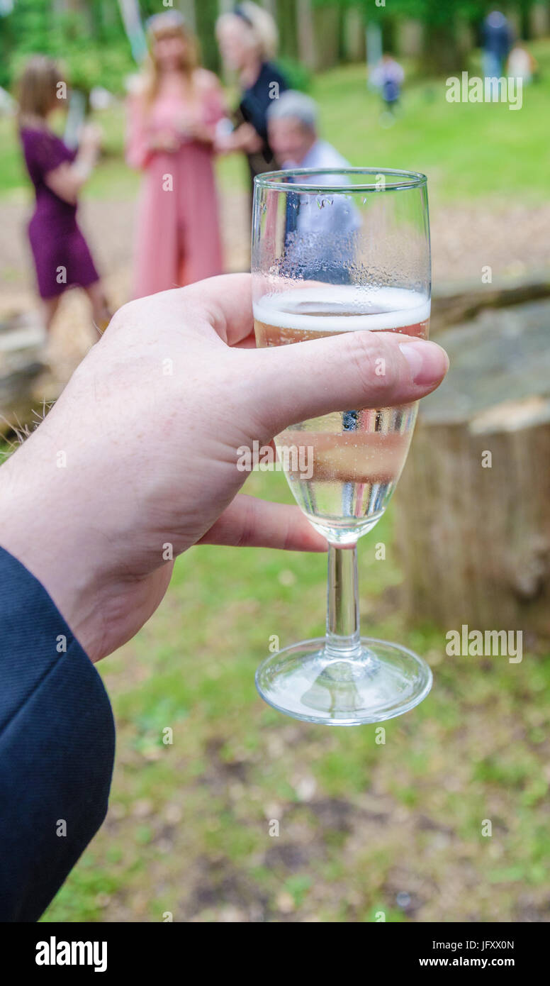A male hand holding a glass of prosecco at a wedding reception. Stock Photo