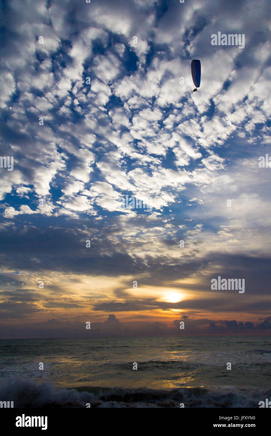 Microlight flying at sunset on Bang Tao beach against a mackerel sky background Stock Photo