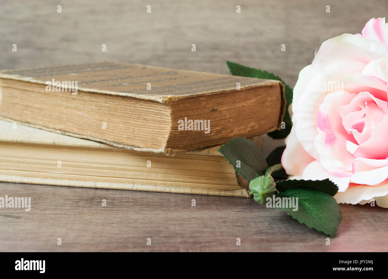 Old books and flower rose on a wooden background. Romantic floral frame background. Picture of a flowers lying on an antique book. Flowers on vintage  Stock Photo